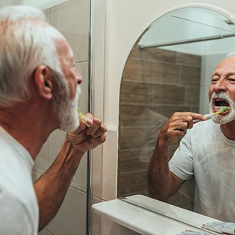 mature man brushing teeth for cost of dental implants in Zionsville 