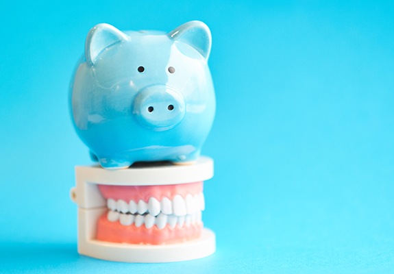 Model smile and piggy bank representing the cost of treating dental emergencies