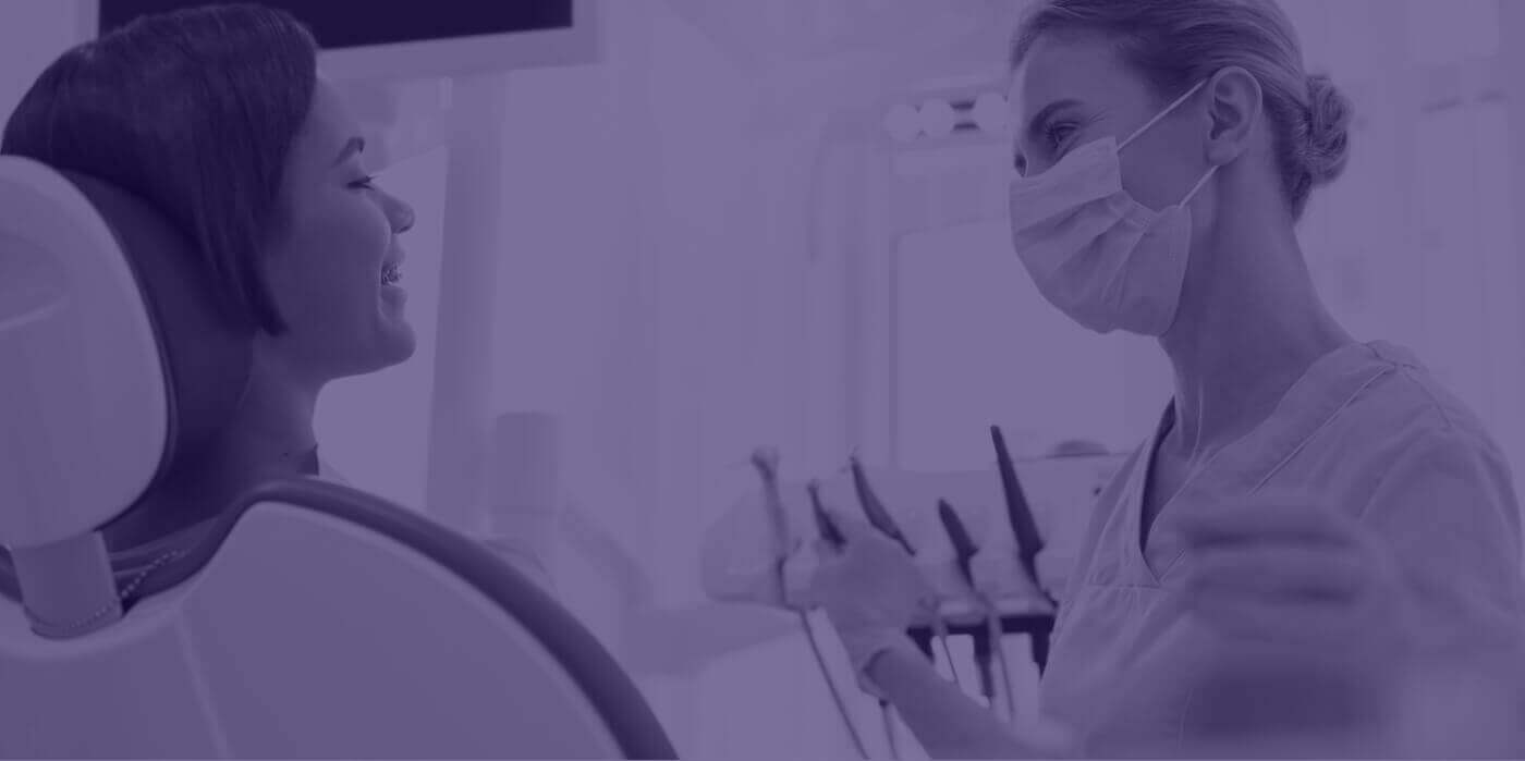 Dental team member talking to young woman in dental chair