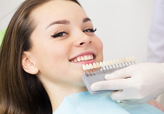 Woman's smile compared with porcelain veneers color chart