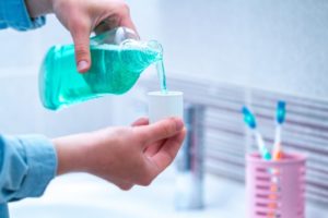 Hand pouring green mouthwash into lid over sink