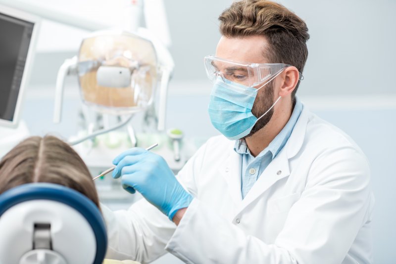 A dentist wearing a face mask, gloves, and protective eyewear while caring for a patient