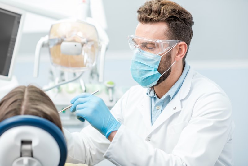 A dentist wearing a face mask, gloves, and protective eyewear while caring for a patient