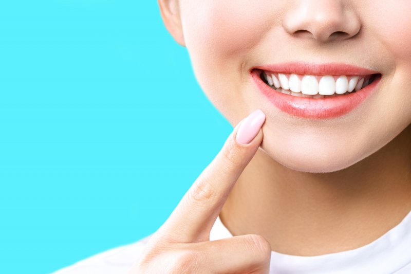 a woman pointing to her whiter, brighter teeth after undergoing a whitening treatment