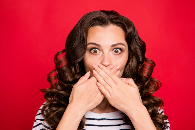 a young woman with dark, curly hair holding her hands over her mouth to hide her lost dental crown