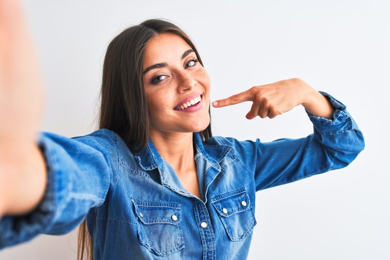 a woman wearing a blue denim blouse and pointing to her whiter, brighter smile