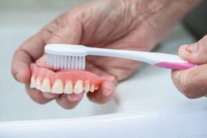 Person brushing their dentures over a sink